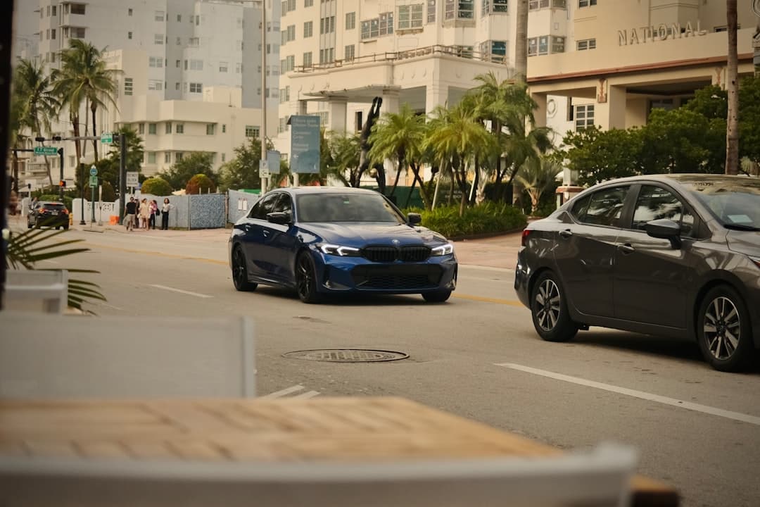 Blue car and grey car on a Miami street, with palm trees and white buildings.